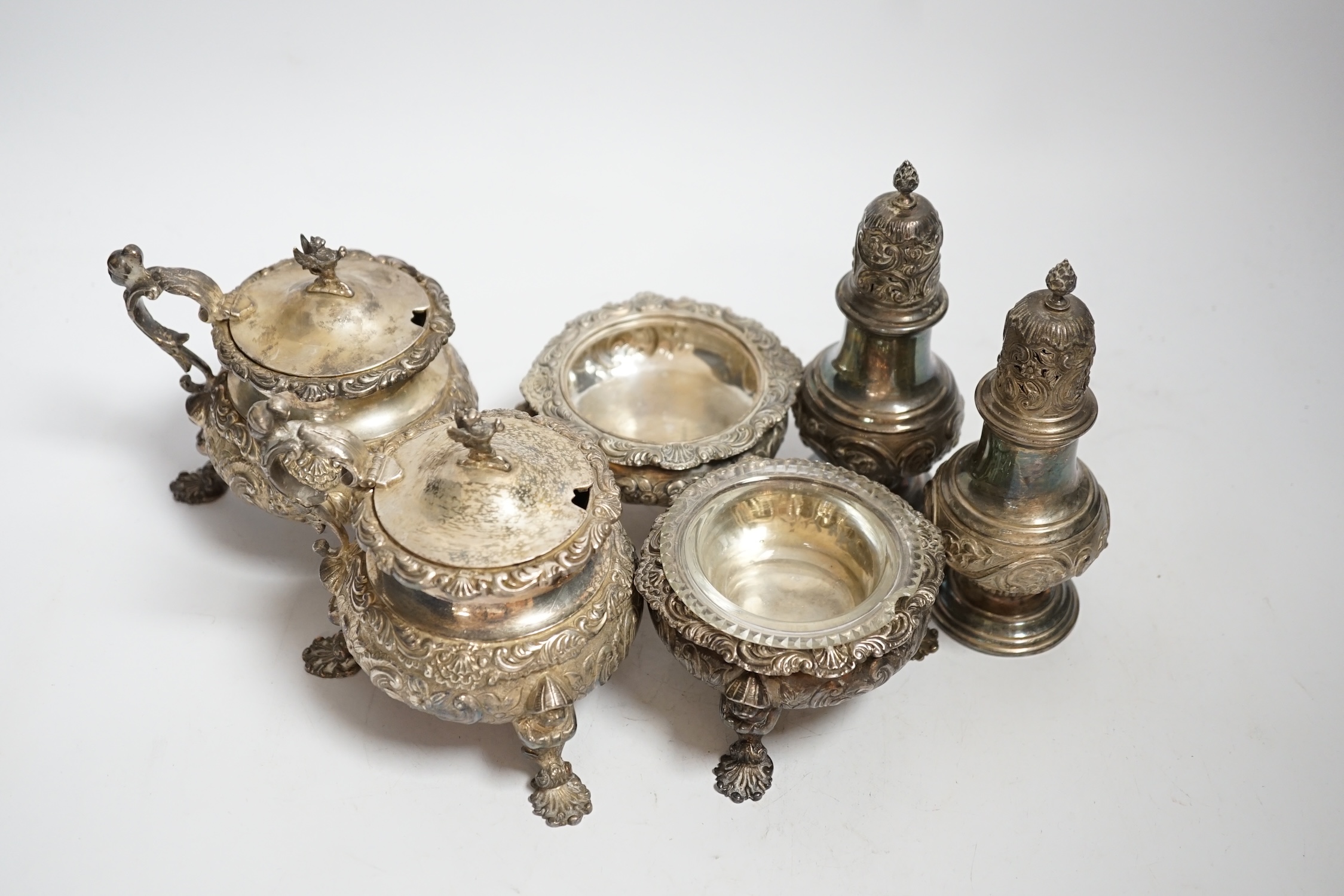 An ornate Edwardian silver four piece condiment set, with chinoiserie decoration by William Comyns, comprising two mustard pots and two salts, one with glass liner and a pair of similar pepperettes, all London, 1906, sal